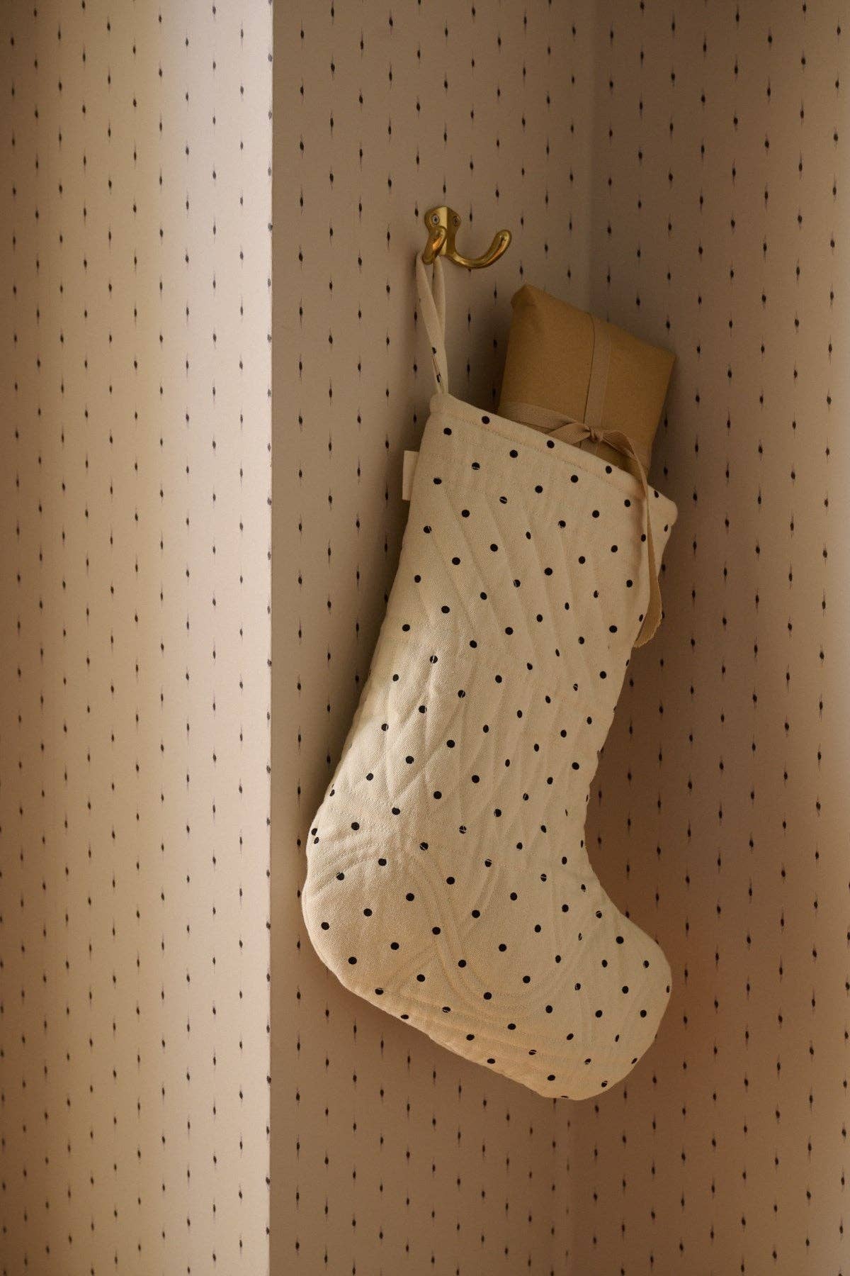 Weiß-schwarz gepunktete Weihnachtssocke befüllt mit einem eingepackten Geschenk.