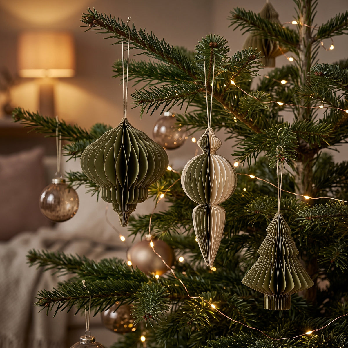 Die grünen Ornamente aus Papier hängen an den Zweigen eines Christbaums im Wohnzimmer, der mit einer Lichterkette geschmückt ist.