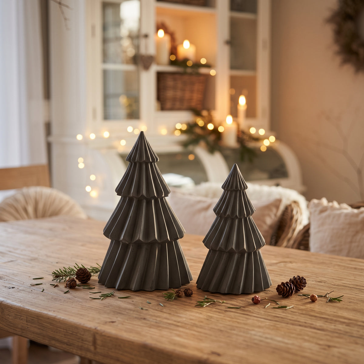 Schwarze Stewalin-Tannenbäume stimmungsvoll arrangiert auf einem rustikalen Holztisch neben Kerzenlicht im weihnachtlich dekorierten Esszimmer.
