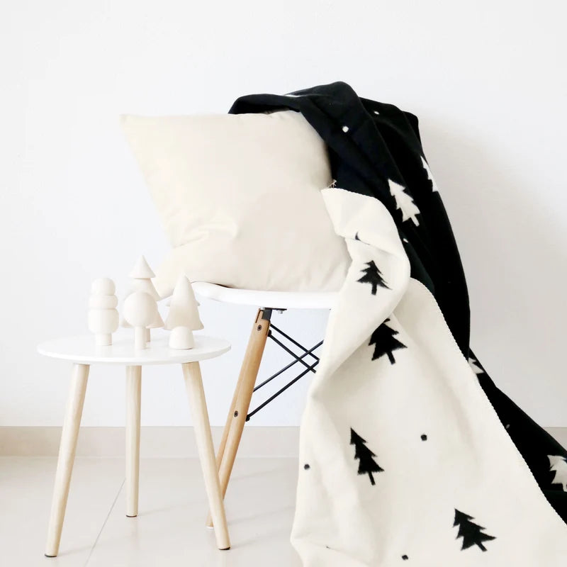 Kuscheldecke Smilla (150x200 cm) gemütlich drapiert auf einem hellen Stuhl im minimalistischen Skandi-Wohnzimmer.