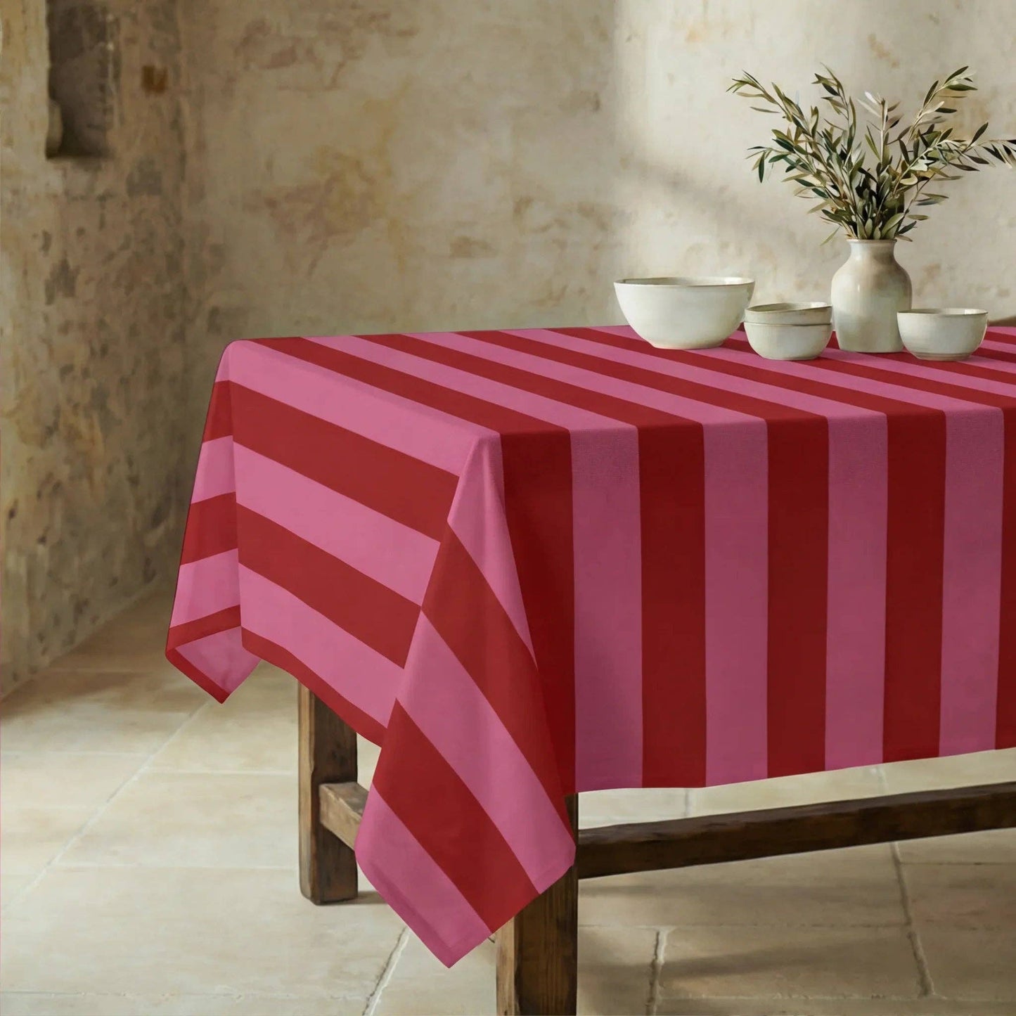 Die sommerlich gestreifte Tischdecke einladend gedeckt mit heller Keramik und einer Vase mit Olivenzweigen.