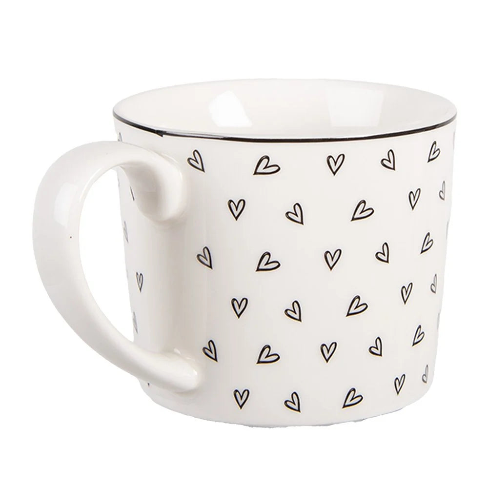 Nahaufnahme der weißen Tasse mit Fokus auf das feine Porzellan und das detaillierte schwarze Herzchen-Muster.