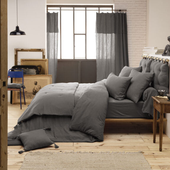 Stilvoll dekoriertes Bett mit der dunkelgrauen Tagesdecke, Kissen und einer gemütlichen Decke im modernen Schlafzimmer.