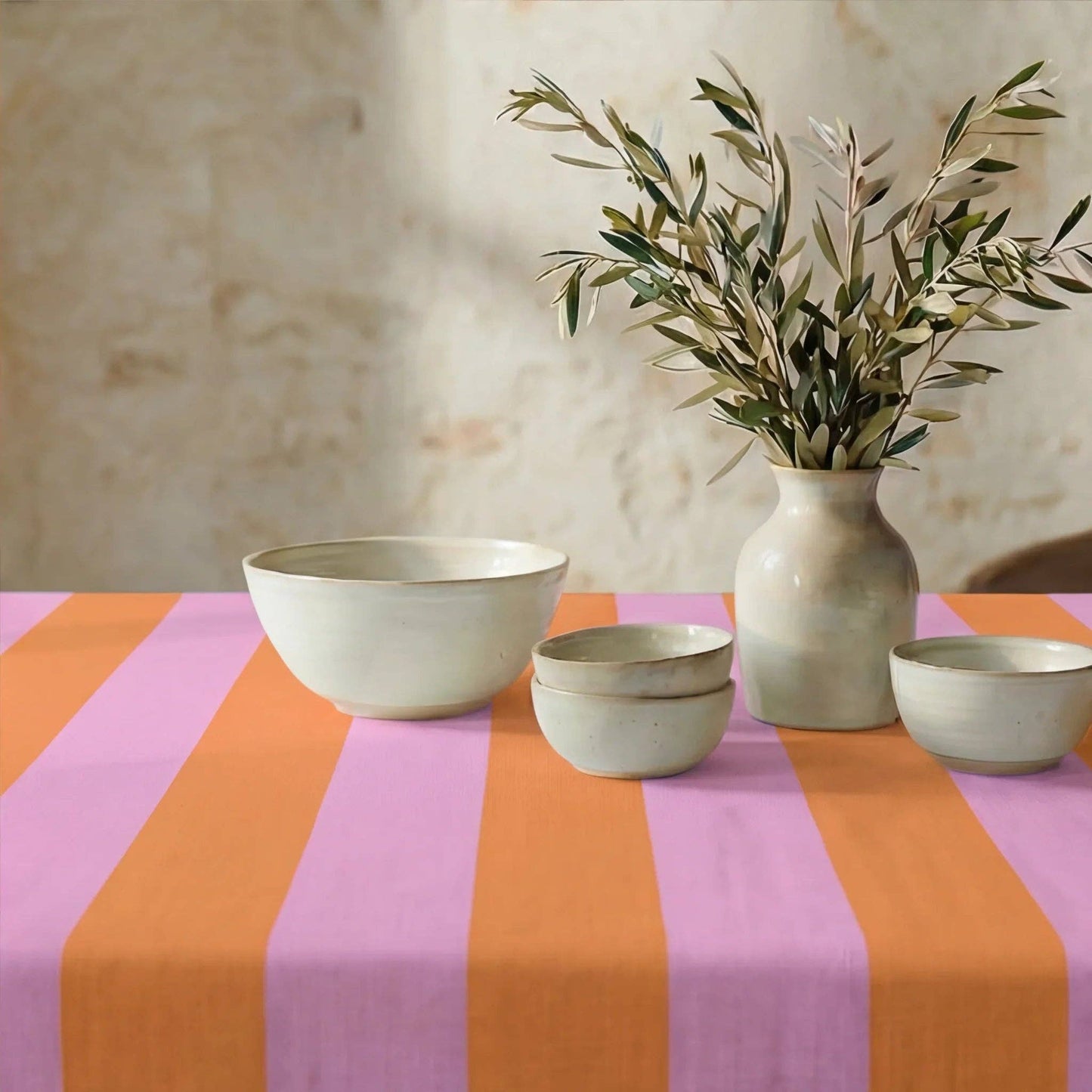 Die sommerlich gestreifte Tischdecke einladend gedeckt mit heller Keramik und einer Vase mit Olivenzweigen.