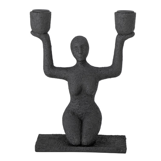 Kerzenhalter Lucie sitzende Frau in Schwarz in der Gesamtansicht vor hellem Hintergrund.