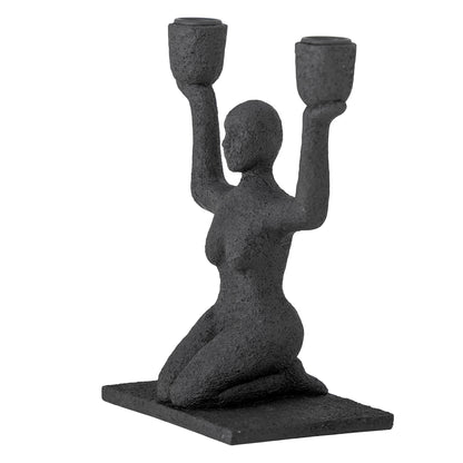 Kerzenhalter Lucie sitzende Frau in Schwarz in der seitlichen Ansicht vor hellem Hintergrund.