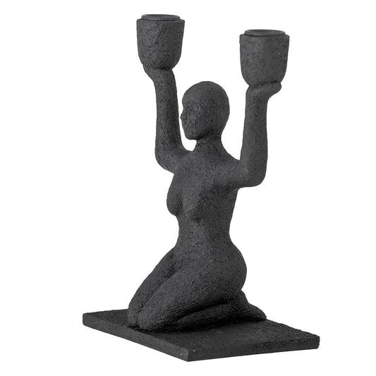 Kerzenhalter Lucie sitzende Frau in Schwarz in der seitlichen Ansicht vor hellem Hintergrund.