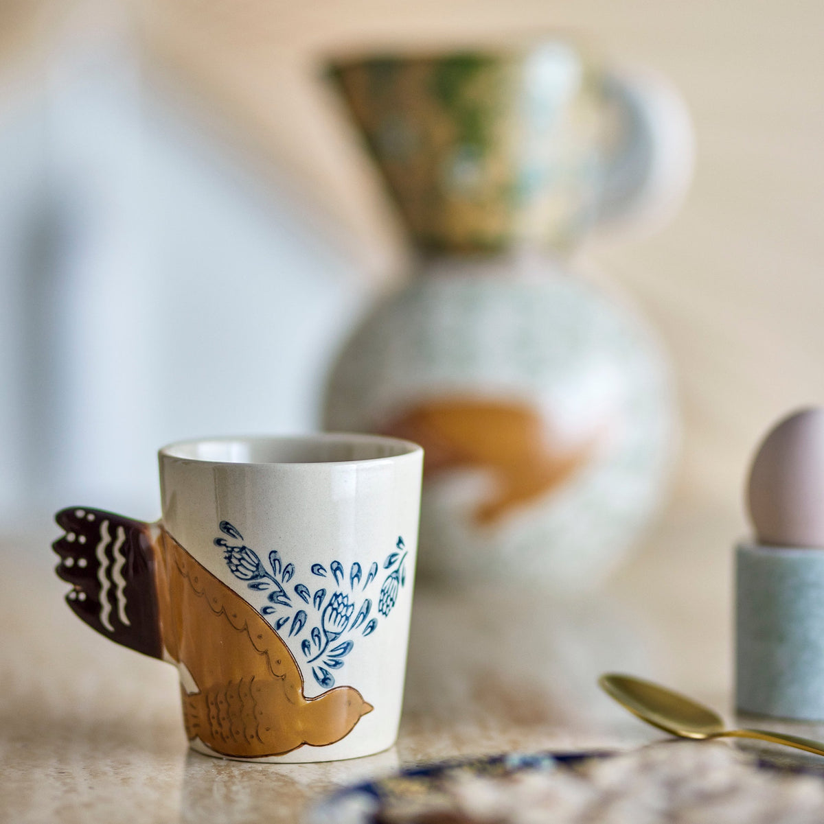 Vogel-Tasse aus Steingut auf einer Steinplatte am Frühstückstisch, der mit Frühstück und Ei gedeckt ist.
