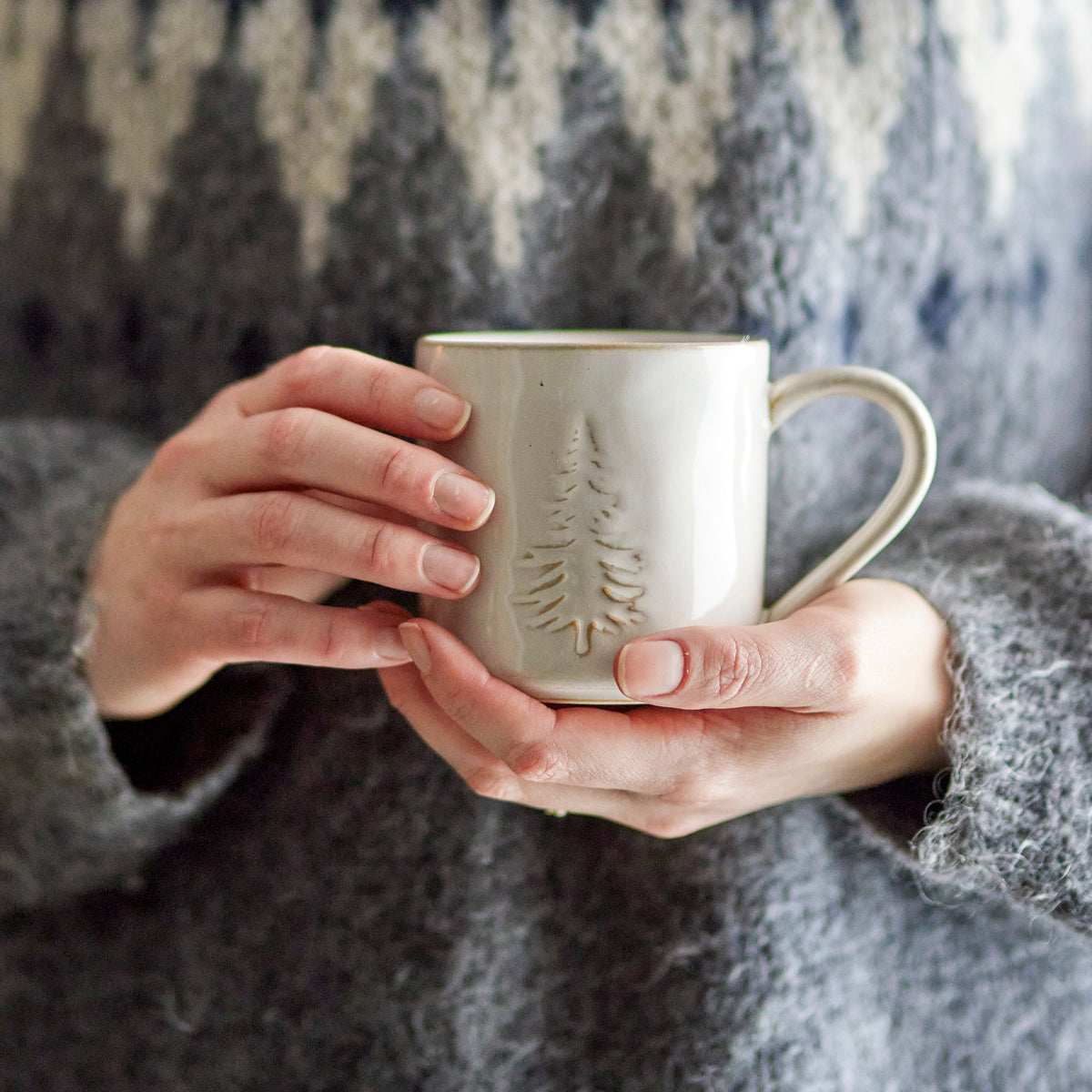 Tasse Tannenbaum aus Steingut mit geprägtem Tannenbaummuster wird von zwei Händen gehalten.