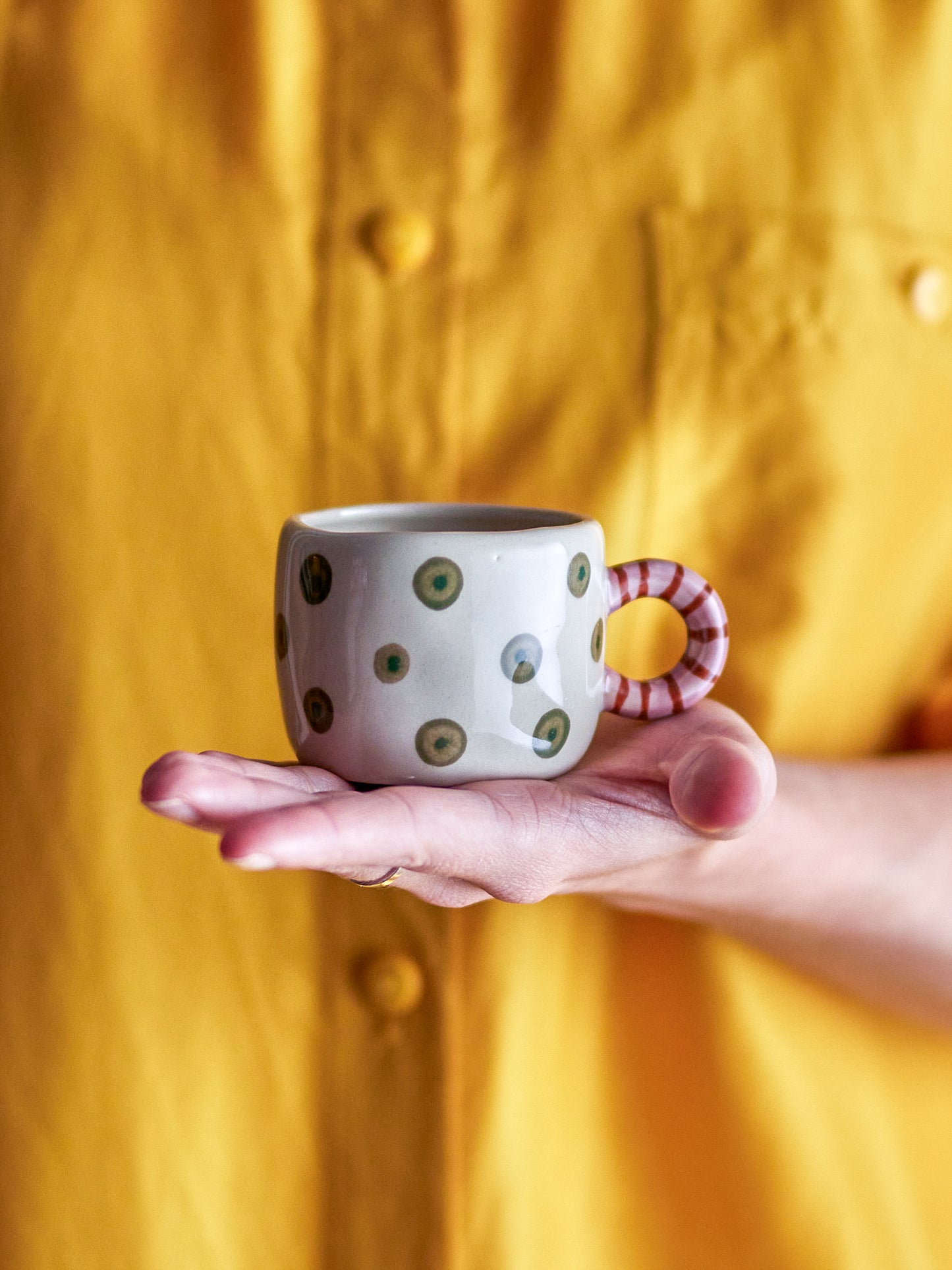 Nahaufnahme des gestreiften Henkels und der fröhlich grünen Punkte auf der Steingut-Tasse.