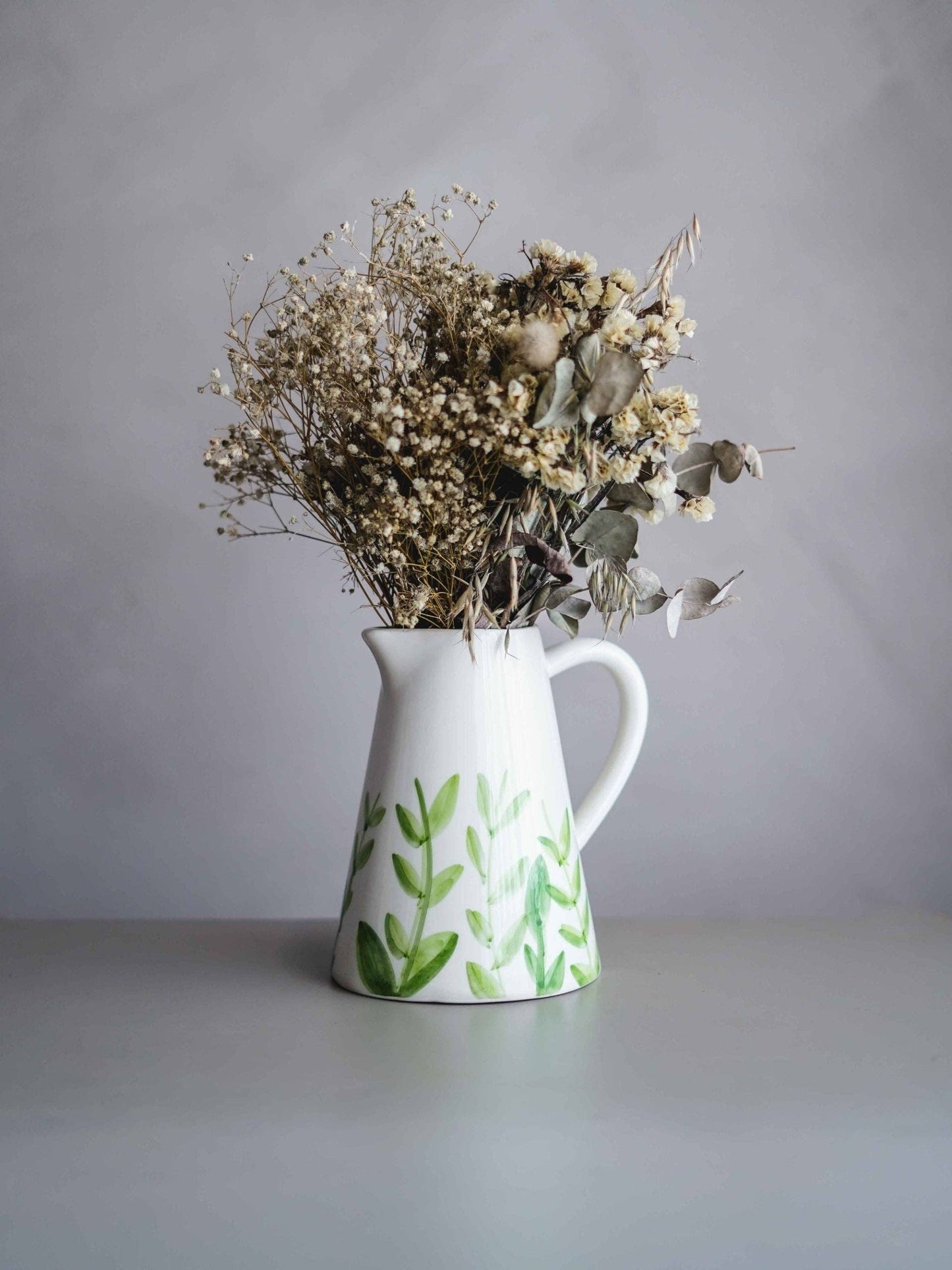 Keramikvase gefüllt mit getrockneten Zweigen auf einem grauen Tisch.
