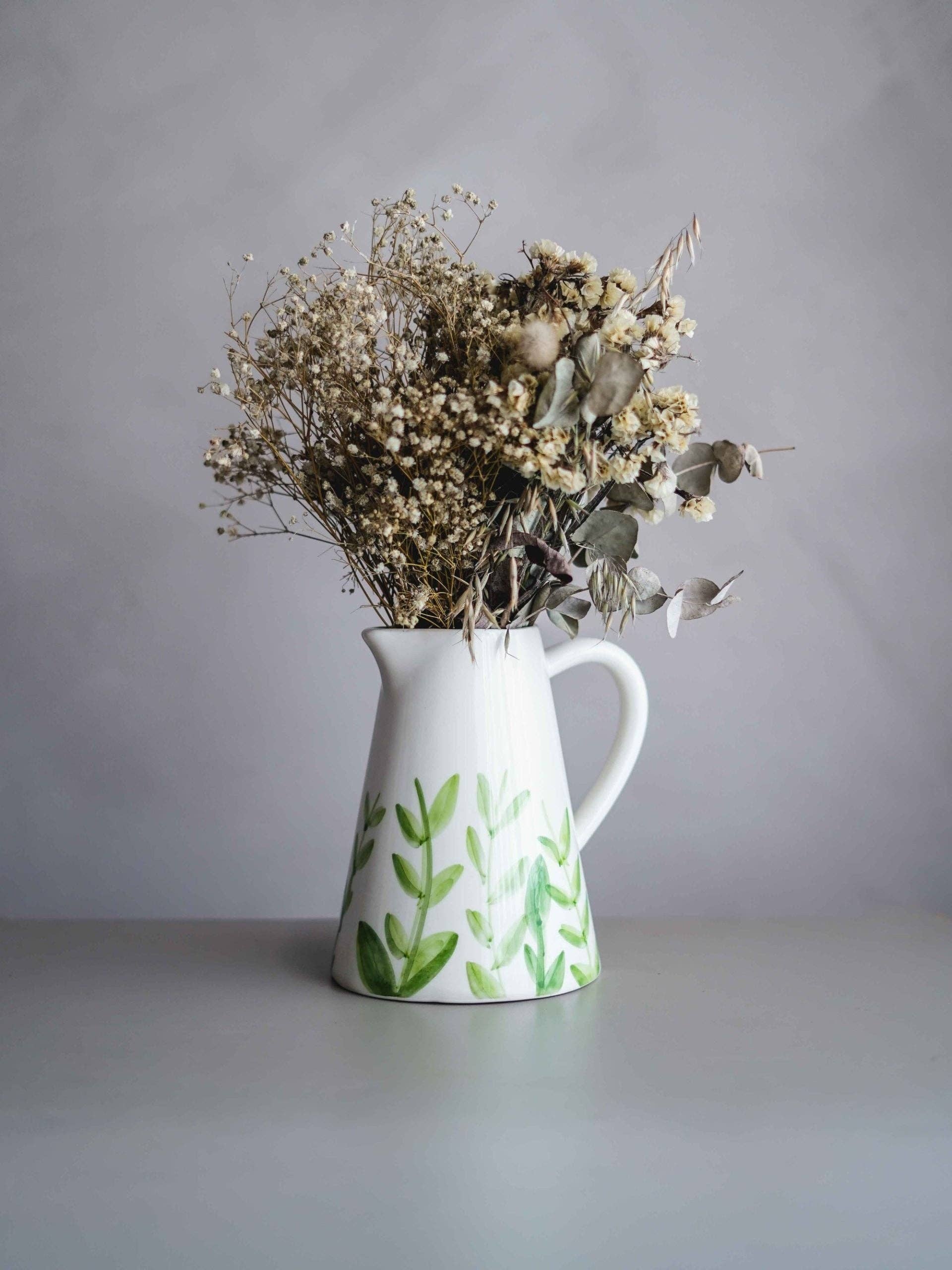 Keramikvase gefüllt mit getrockneten Zweigen auf einem grauen Tisch.