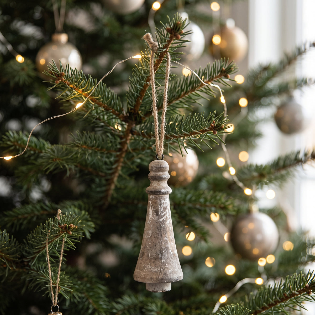 Silberner Weihnachtsanhänger aus Holzwerkstoff (6x16 cm) aufgehängt an einem geschmückten Tannenbaum.