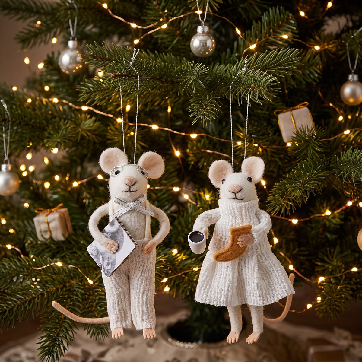 Maus-Anhänger an Tannenzweigen eines Christbaums aufgehängt, der mit einer Lichterkette und weihnachtlichem Baumschmuck dekoriert ist.
