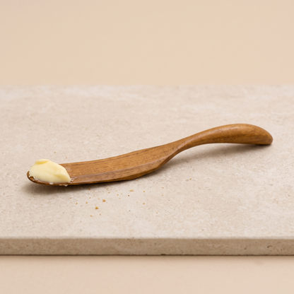 Nahaufnahme der natürlichen Holzmaserung und geschwungenen Form des Teak-Buttermessers.