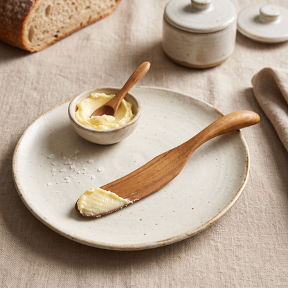 Teakholz-Buttermesser dekoriert auf einem weißen Teller mit frischem Landbrot und Butter.