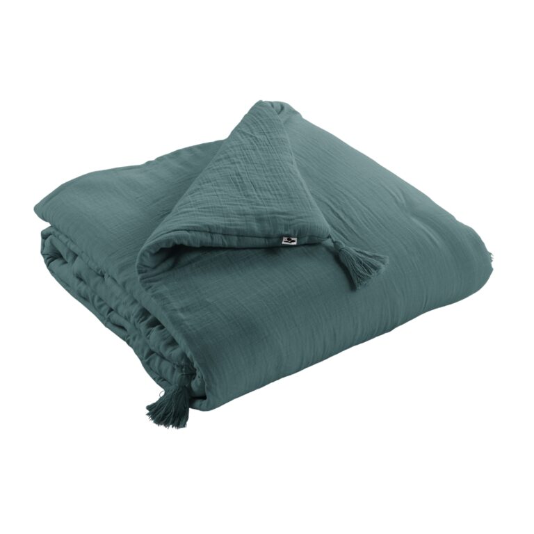Nahaufnahme der blauen Baumwoll-Struktur und der Ecken-Pompoms der Tagesdecke.