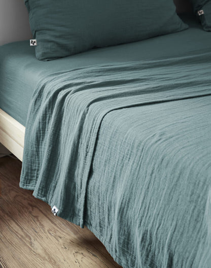 Die cremefarbene XXL-Baumwolldecke blau als stilvoller Sofabezug im Schlafzimmer auf einem weißen Bett.