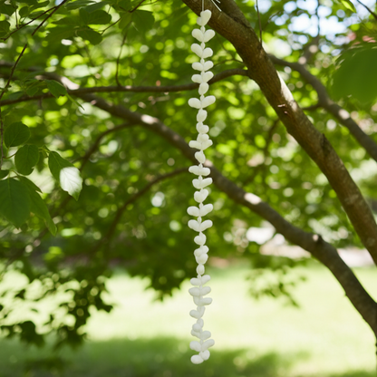 Die minimalistische weiße Muschelkette als natürlicher Akzent an einem Baum hängend.