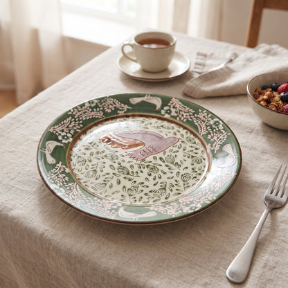 Teller Hezha in grün mit Vogel und Blüten-Muster auf einem Frühstückstisch mit einer hellen Leinen-Tischdecke.