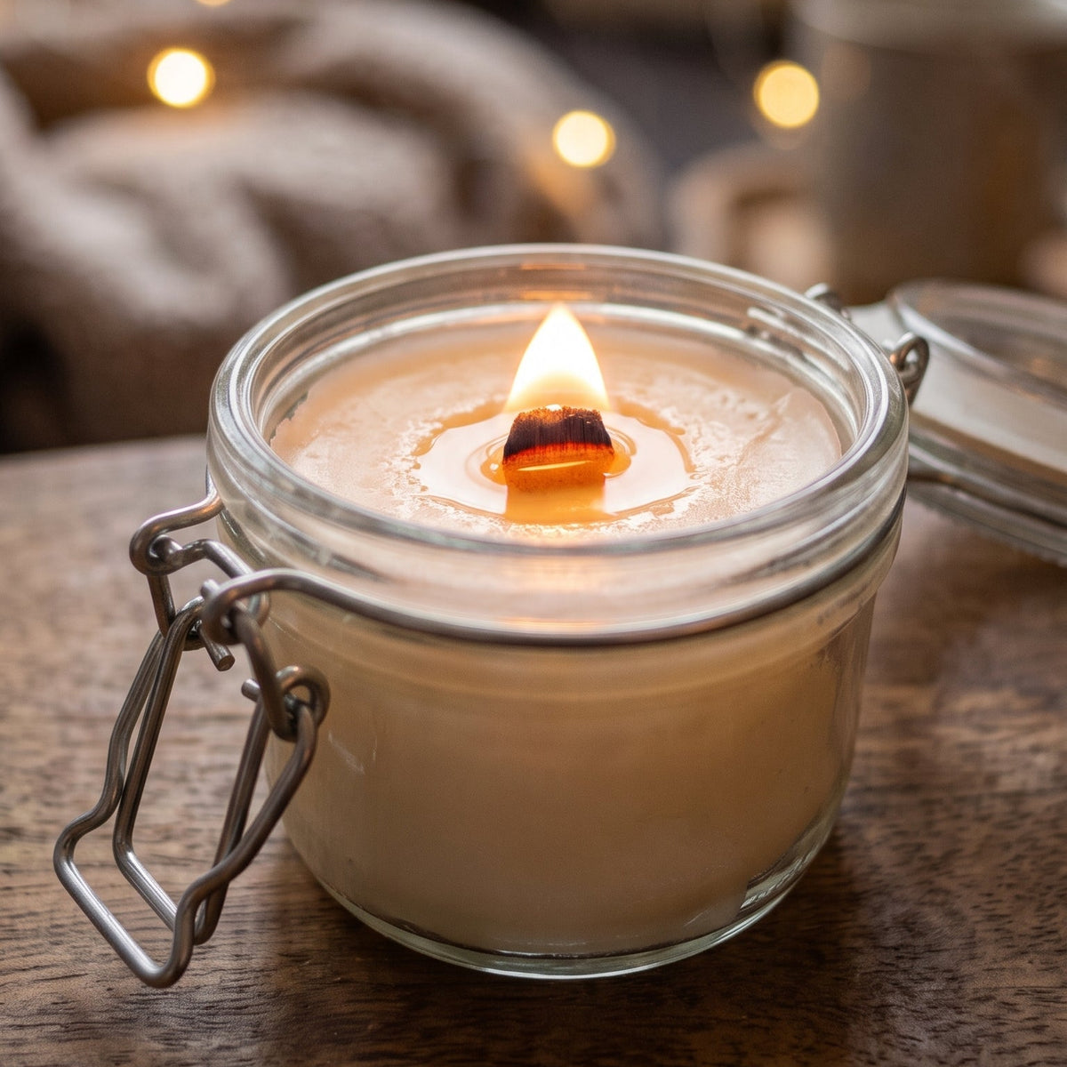 Knisterkerze mit Holzdocht mit Flamme auf einem dunklen Holztisch im gemütlichen Wohnzimmer.