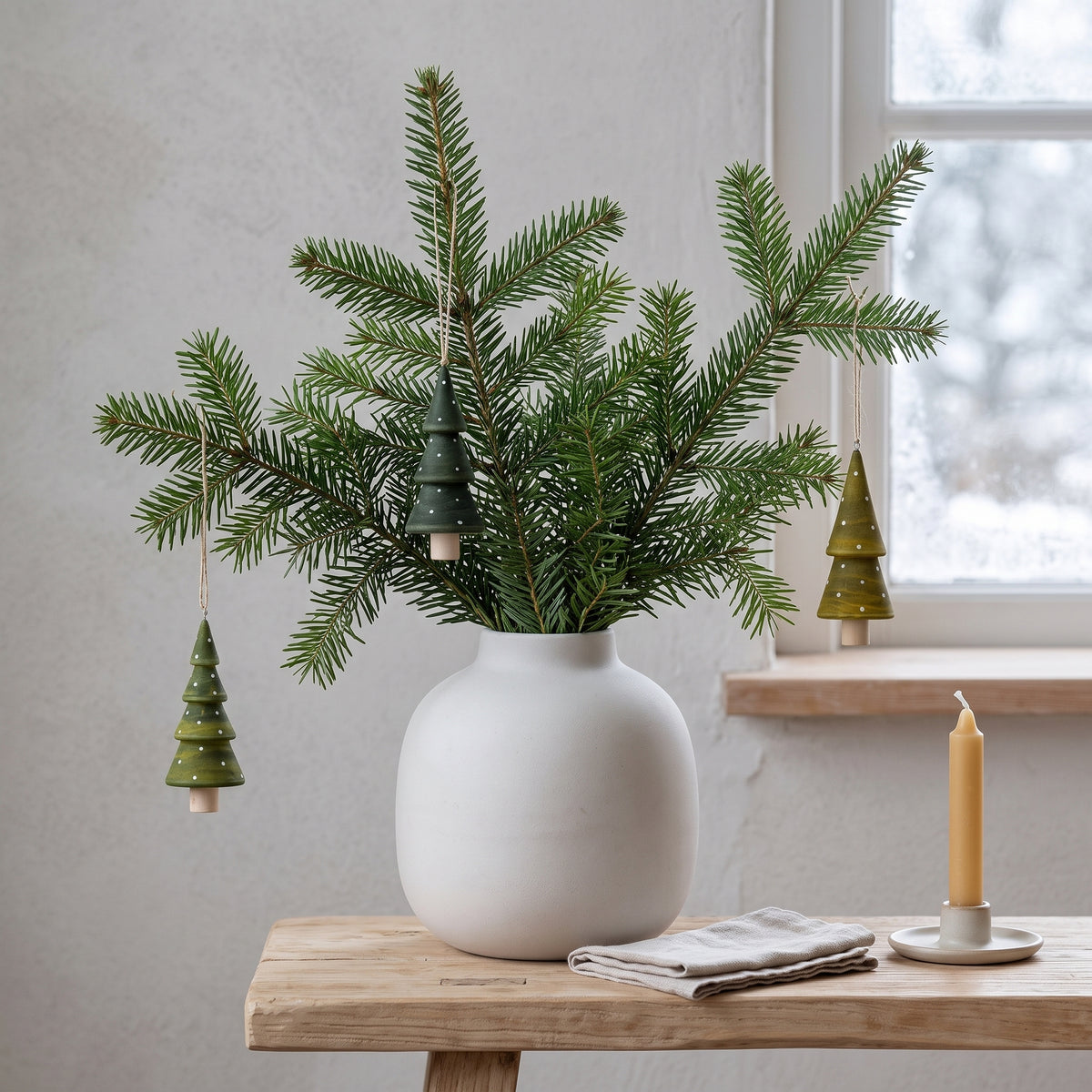  Die kleinen grünen Holz-Tannenbäume stimmungsvoll an Tannenzweigen in einer Vase für eine minimalistische, skandinavische Winterdekoration arrangiert.