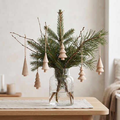 Die kleinen Holz-Tannenbäume stimmungsvoll an Tannenzweigen in einer Vase für eine minimalistische, skandinavische Winterdekoration arrangiert.