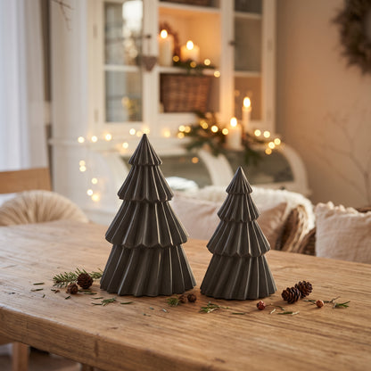 Schwarze Stewalin-Tannenbäume stimmungsvoll arrangiert auf einem rustikalen Holztisch neben Kerzenlicht im weihnachtlich dekorierten Esszimmer.