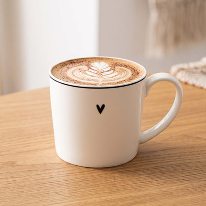 Weiße Tasse mit Herzmotiv gefüllt mit Cappuccino auf einem Holztisch.