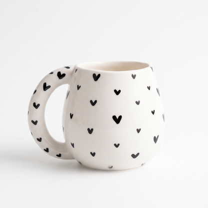 Bauchige weiße Keramik-Tasse mit schwarzen Herzen in der Gesamtansicht vor hellem Hintergrund.