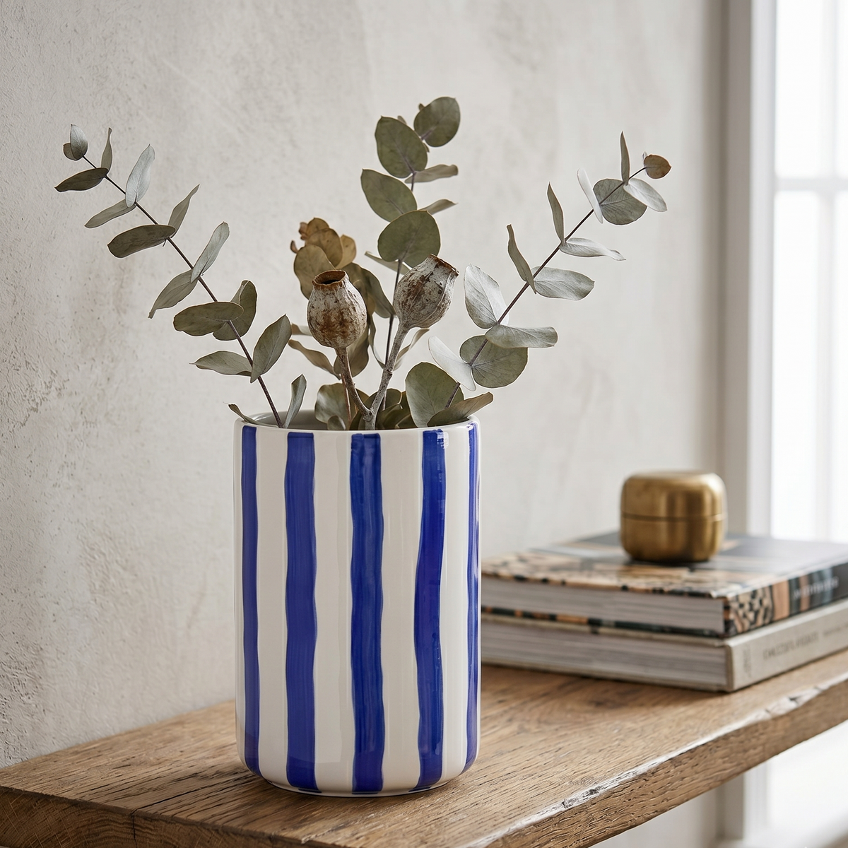 Die minimalistische gestreifte Keramikvase gefüllt mit getrockneten Zweigen als stilvoller und frischer Blickfang im Wohnbereich.