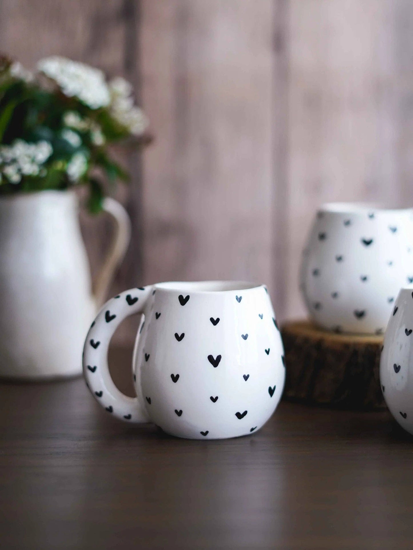 Die weiße Tasse mit schwarzen Herzen steht auf einem gemütlich gedeckten Holztisch.