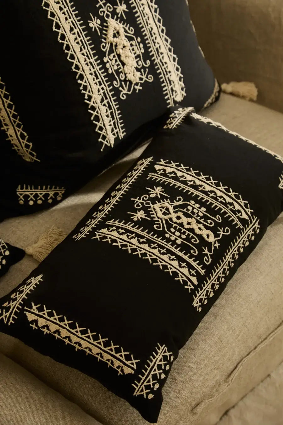 Der bestickte Boho-Kissenbezug Traste dekorativ arrangiert auf einer hellen Couch.
